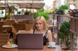 © Mikhail - young blonde woman sitting with a laptop on summer terrace. front view