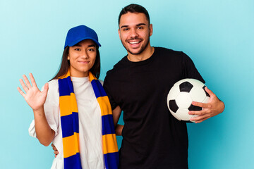 Wall Mural - Young mixed race couple cleaning home isolated on blue background smiling cheerful showing number five with fingers.