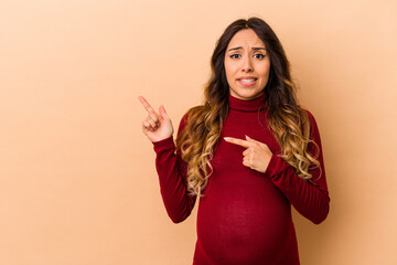 Wall Mural - Young mexican pregnant woman isolated on beige background shocked pointing with index fingers to a copy space.