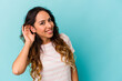 © Asier - Young mexican woman isolated on blue background trying to listening a gossip.