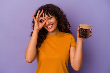 Wall Mural - Young mixed race woman holding a coffee beans bottle isolated on purple background excited keeping ok gesture on eye.