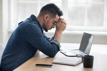 Wall Mural - Depressed arab man sitting in front of laptop, office interior