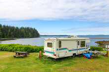 Vacation - Holiday In The Campground. The View On The Picnic Table And The White RV Parked On The Shore In Alder Bay. The Beautiful View On The Ocean And Woods. 