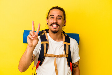 Young caucasian hiker man with long hair isolated on yellow background joyful and carefree showing a peace symbol with fingers.