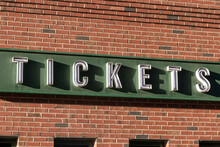 Ticket Window Sign In White Text, With A Green And Brick Background.
