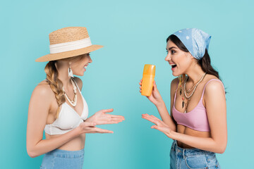 Sticker - Smiling women in tops pointing at sunscreen isolated on blue.