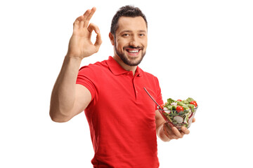 Wall Mural - Young man in a red t-shirt holding a fresh salad in a bowl and gesturing good sign