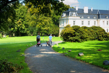 Summer landscape - two golfers after the game, next to chateau of Silgerovice. Czech Republic