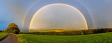 Beautiful Full Rainbow On The Blue Sky Above The Green Field And Trees