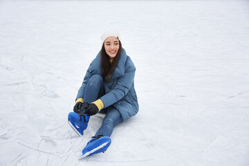 Wall Mural - Woman adjusting figure skate while sitting on ice rink. Space for text