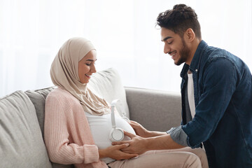 Wall Mural - Loving Arab Husband Placing Wireless Headphones On Pregnant Wife's Belly