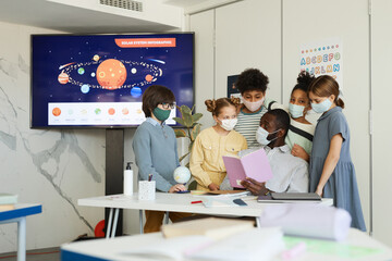 Portrait of diverse group of children and teacher wearing masks in school classroom, covid safety measures, copy space