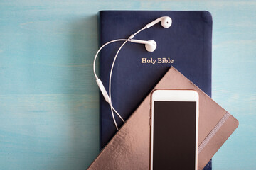 Bible with journal, smartphone and earbuds on blue background with copy space