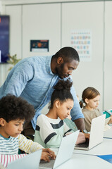 Wall Mural - Side view portrait of male teacher helping children using computers in IT class