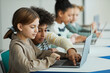 © Seventyfour - Side view at diverse group of children sitting in row at school classroom and using laptops