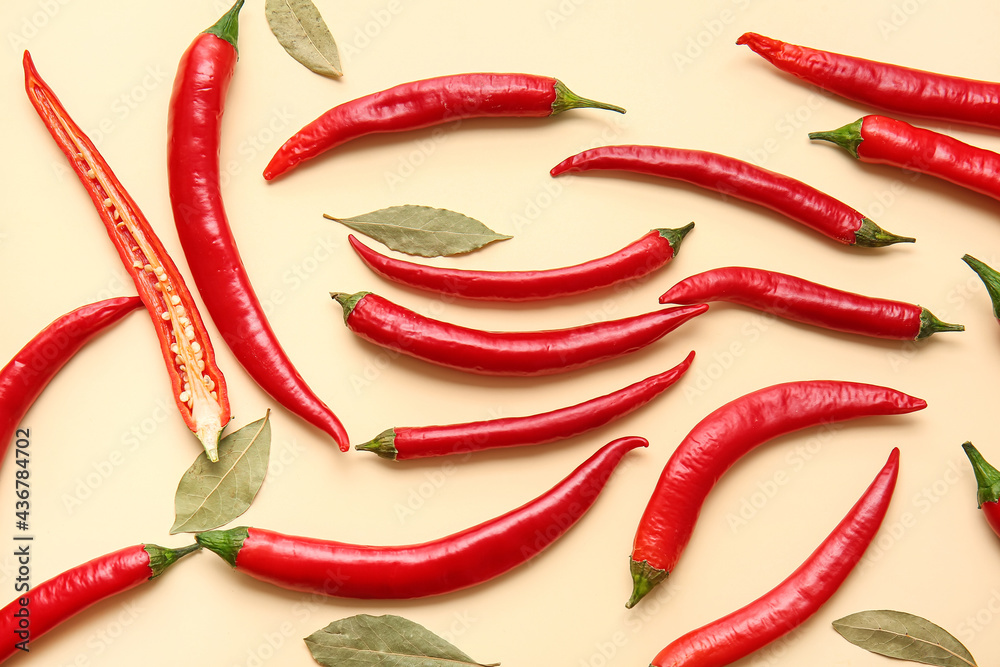 Hot chili peppers and bay leaves on color background