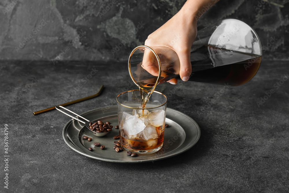 Pouring of cold brew coffee from jug into glass on grunge background - obrazy, fototapety, plakaty 