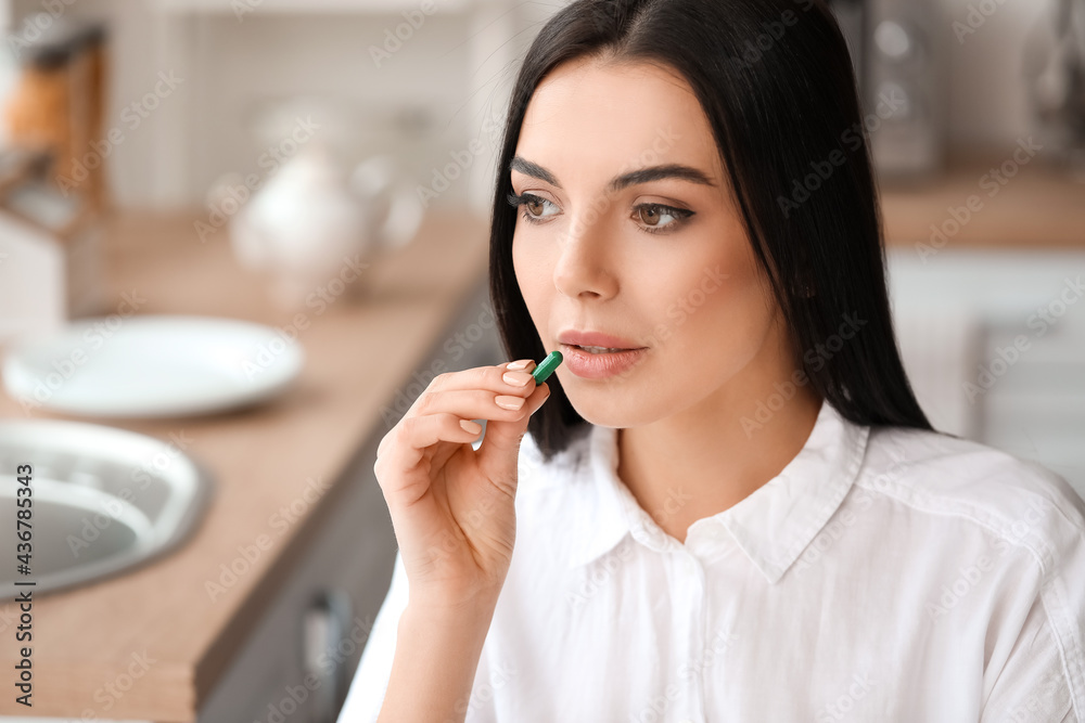 Beautiful young woman taking pills in kitchen