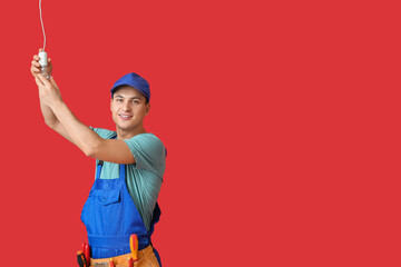 Young electrician screwing light bulb on color background