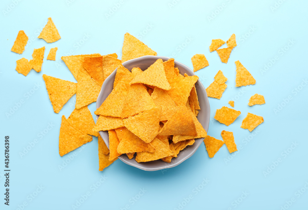 Bowl with tasty nachos on color background