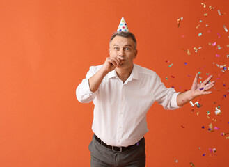 Happy mature man in party hat and with noisemaker on color background