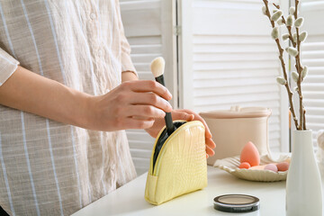 woman with cosmetic bag and brush in room