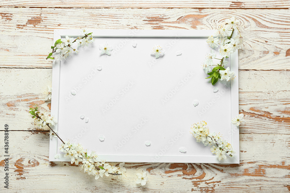 Blank frame and beautiful blooming branches on light wooden background