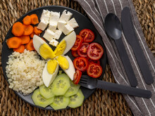 Dark Plate On Straw Mat With Plain Rice, Chopped Boiled Egg, Cherry Tomatoes, Sliced Cucumbers, Carrots On Wheels And Greek Feta Cheese Cubes