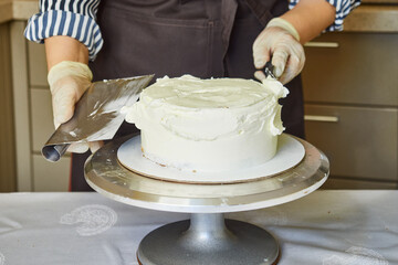 Female hands aligns cake cream with a metal spatula. Homemade baking.