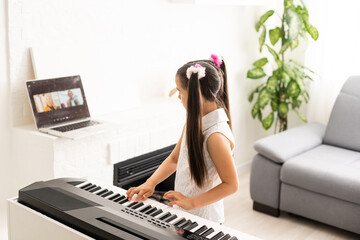 Wall Mural - Homeschool little young kid girl learning piano from computer connecting to internet music online class by school teacher. New normal lifestyle and education, student study at home concept.