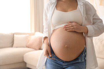 Poster - Pregnant young woman touching belly at home, closeup. Space for text