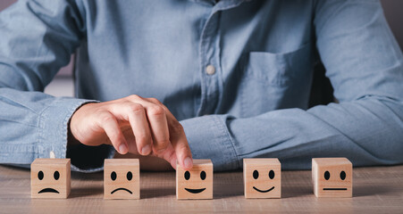 Hand of a businessman chooses a smiley face on wood block cube.Customer services best excellent business rating experience. Satisfaction survey concept.