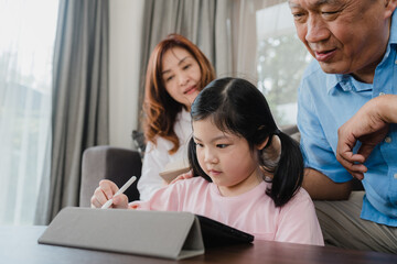 Wall Mural - Asian grandparents and granddaughter video call at home. Senior Chinese, grandpa and grandma happy with girl using mobile phone video call talking with dad and mom lying in living room at home.