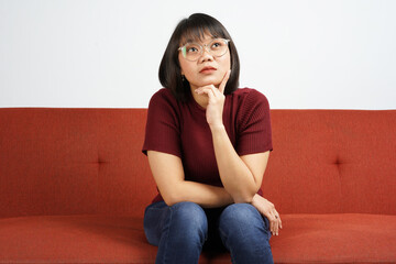 Thinking gesture Young beautiful Asian women dress red shirt and jeans sitting on red couch