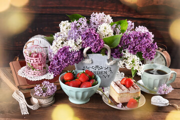 cake with strawberry and cup of coffee on the table with bunch of lilac