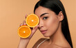 canvas print picture - Portrait of Asian girl with shining clean skin of face holding orange halves in white underwear isolated on beige background. Vitamin C cosmetics concept