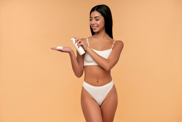 Wall Mural - Young asian woman in white lingerie with shining skin with bottle of facial foam.isolated on a beige background. Facial skin care concept. Beauty.