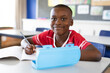 © WavebreakMediaMicro - Portrait of african american boy smiling while sitting on his desk in the class at school