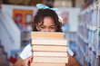 Portrait of happy african american schoolgirl carrying stack of books in school library