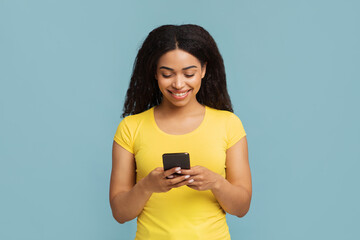 Great app. Interested african american woman with smartphone in hands standing on blue background