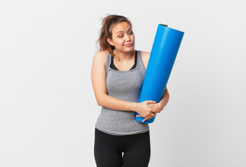 Wall Mural - young pretty woman shrugging, feeling confused and uncertain and holding a yoga mat