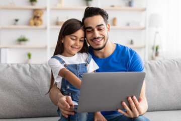 Wall Mural - Smiling dad and daughter sitting on couch, using pc