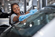 © Roman - Female african auto mechanic cleaner is cleaning car window glass with blue rag, side view on adorable black woman in car service, working alone, washing vehicle