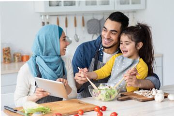 Wall Mural - Happy Islamic Family Checking Recipe On Digital Tablet While Cooking In Kitchen