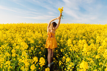 Attractive woman with bouquet posing in blooming rapeseed field with sunset.