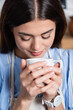 © LIGHTFIELD STUDIOS - portrait of smiling young adult woman smelling aroma of coffee in white cup on blurred background