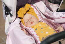 A Little Newborn Girl In A Yellow Beanie Sleeps In A Pink Stroller Sunbathing In The Sun In The Fresh Air