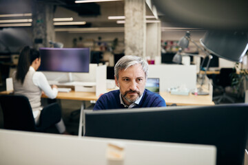 mid adult computer programmer working on desktop pc at corporate office.
