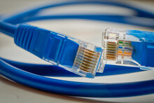 Two Network RJ45 Plugs Of Blue Colour Macro. Blue RJ45 CAT6 Shielded Network Data Internet Cable In Coils And Connectors On Gray Background Shallow DOF