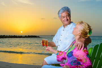 Wall Mural - Romantic older couple at the beach with beach chairs having drinks, champagne, at sunset